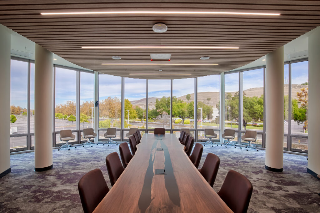 Large conference room with large wood table, chairs, and floor to ceiling windows overlooking an outdoor landscape