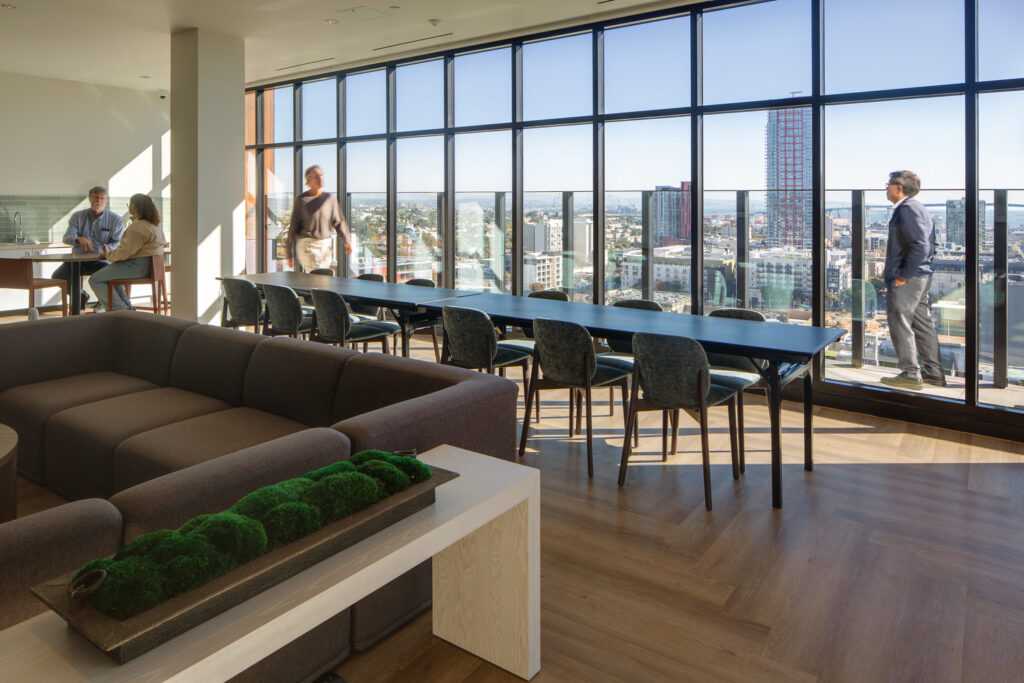 lounge with long table, city views through floor-to-ceiling windows, and people meeting.